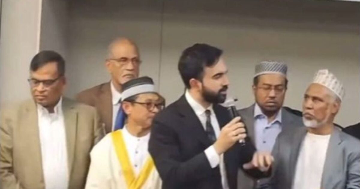Group of men at a conference, with one speaker holding a microphone and engaging the audience, showcasing cultural diversity and community involvement.